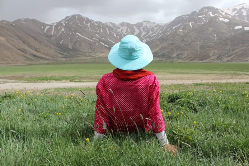 Person sitting on grass field looking at mountains